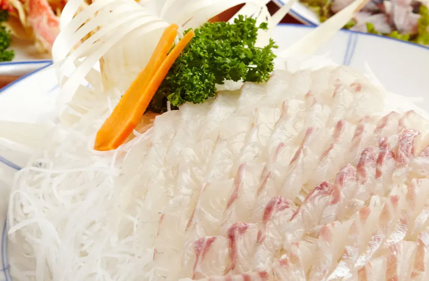 Irisan tipis sashimi Dageumbari (ikan kakap kuning) dihiasi dengan daun parsley, wortel, dan bawang bombay.